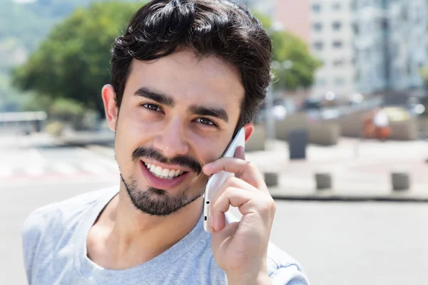 Hispanic guy in a grey shirt at phone in city — Stock Photo, Image