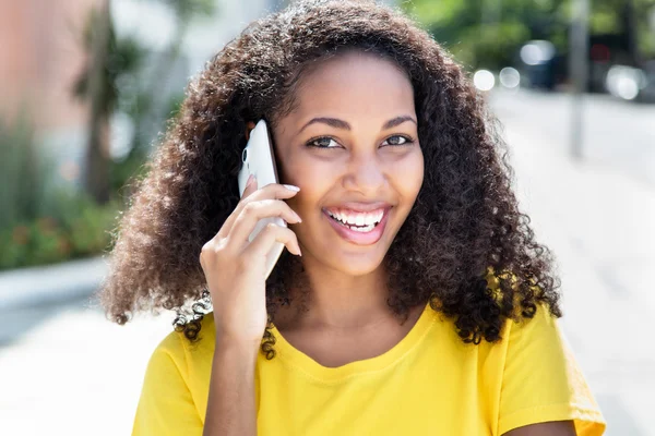 Счастливая женщина с кудрявыми волосами у телефона летом — стоковое фото