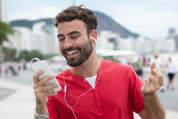 Человек в красной рубашке и мобильнике в городе слушает музыку — стоковое фото