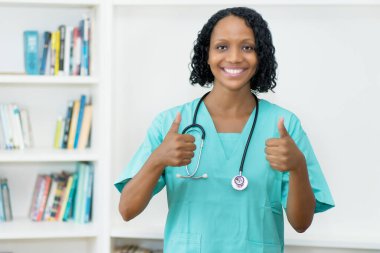 İyimser Afro-Amerikalı olgun hemşire klinikte iki parmağını da gösteriyor.