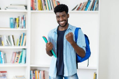 Successful young african american male student with beard at library of university clipart