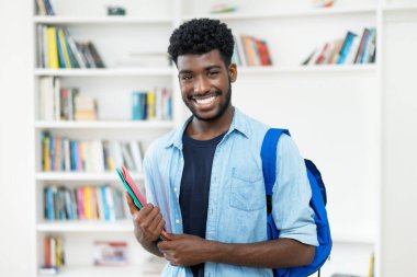 Laughing young african american male student with beard at library of university clipart
