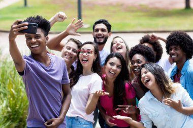 Çok ırklı genç yetişkinler yazın şehrin dışında telefonla çılgınca selfie çekiyorlar.