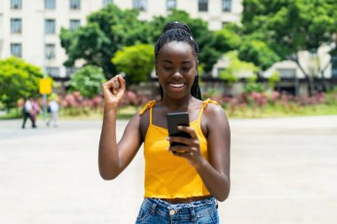 Yazın açık havada telefonla mesaj alan Afro-Amerikalı bir kız.