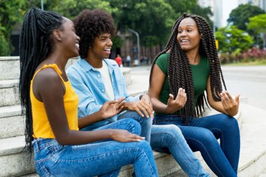 Bir grup Afrikalı Amerikalı erkek ve kadın yetişkin yazın açık havada konuşuyorlar.