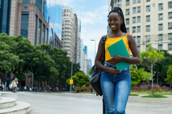 アフリカ系アメリカ人の女子学生が夏に街中でブライドやバックパックを持って笑っています — ストック写真