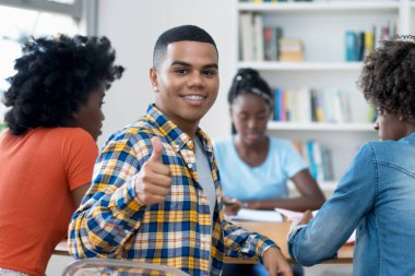 Diş teli takan başarılı İspanyol erkek öğrenci bir grup Amerikalı öğrenciyle üniversite kütüphanesinde eğitim görüyor.