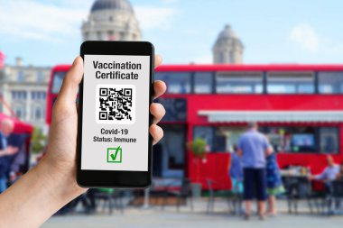 Aşı sertifikalı cep telefonu ekranda ve Londra 'da kırmızı otobüs.