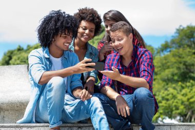 Hispanic influencer with mobile talking with other young adults outdoor in summer in city