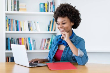 African american female young adult streaming and watching clips and movies at computer at desk at home