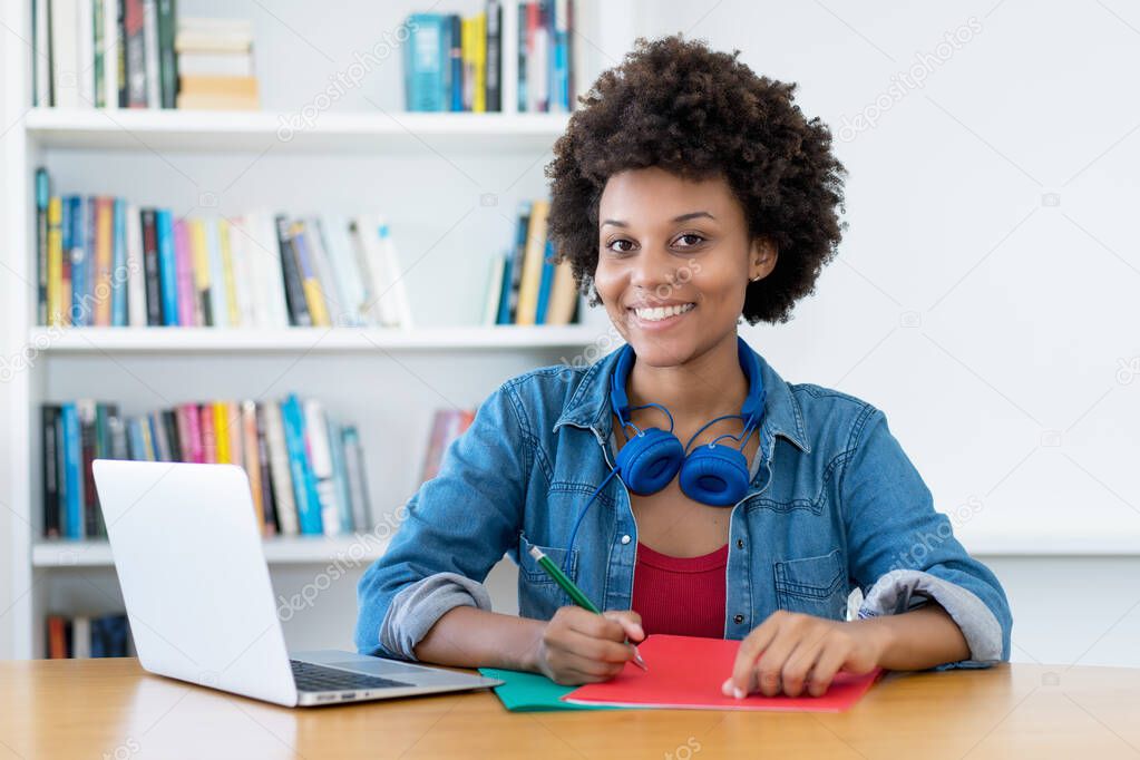 Pretty african american female student learning at desk indoors at library at desk at home