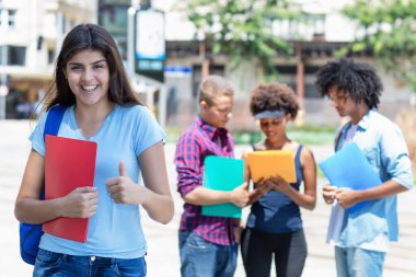 Successful young hispanic female student with group of young adults in summer in city