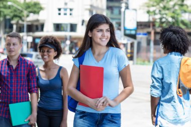 Beautiful young hispanic female student with group of young adults in summer in city