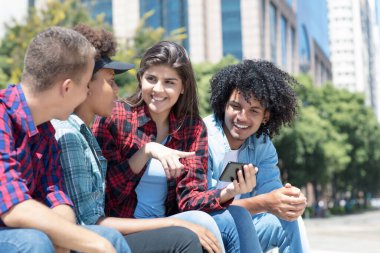 Spanish female influencer showing post on phone to multi ethnic friends outdoor in city in summer