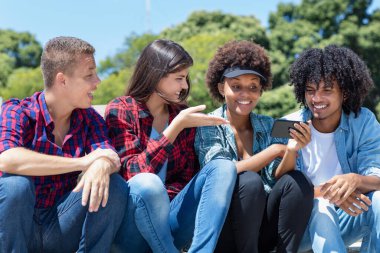 Group of latin and african american young adults watching clip on phone outdoor in city in summer