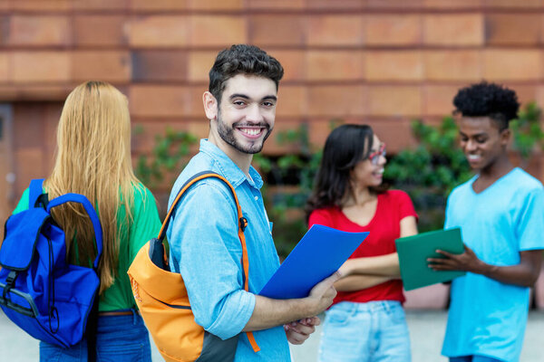 Handsome spanish male student with group of other students outdoor at campus of university