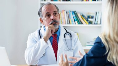 İspanyol erkek doktor klinikteki kadın hastayı dinliyor.