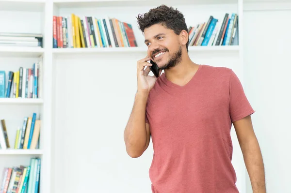 Laughing hispanic hipster man talking with girlfriend at mobile phone indoors at home