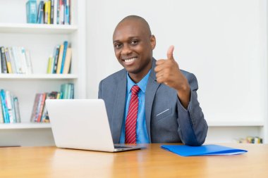 Bilgisayardaki Afrikalı Amerikalı işadamı, başparmağını ofiste gösteriyor.