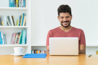 Evde bilgisayar başında sakallı, Latin kökenli, olgun bir adam.