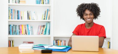 Afro-Amerikan erkek öğrenci gülerek bilgisayar başında fotokopi uzayı ile çalışıyor.