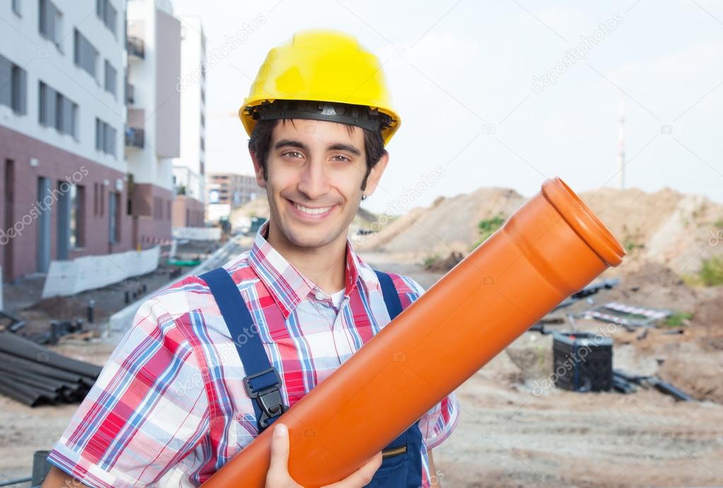 Laughing hispanic construction worker with pipe at building site