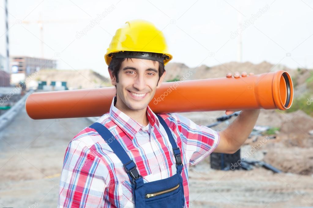 Happy hispanic construction worker with pipe at building site