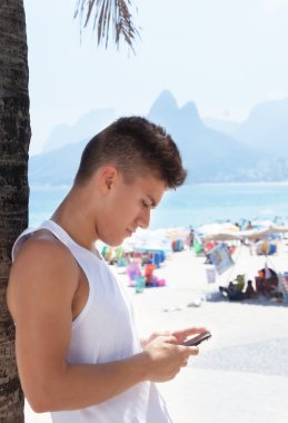 Genç adam plajda telefonuyla mesaj yazma