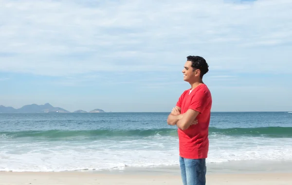 Chico latino de pie en la playa y mirando al océano — Foto de Stock