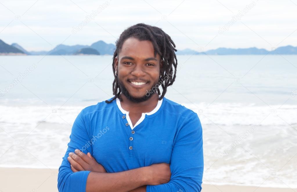 African american guy with dreadlocks and crossed arms at beach