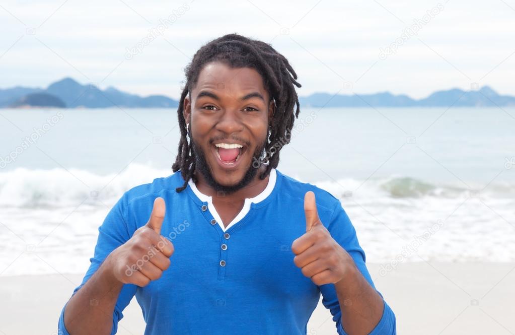 African american guy with dreadlocks at beach showing both thumb