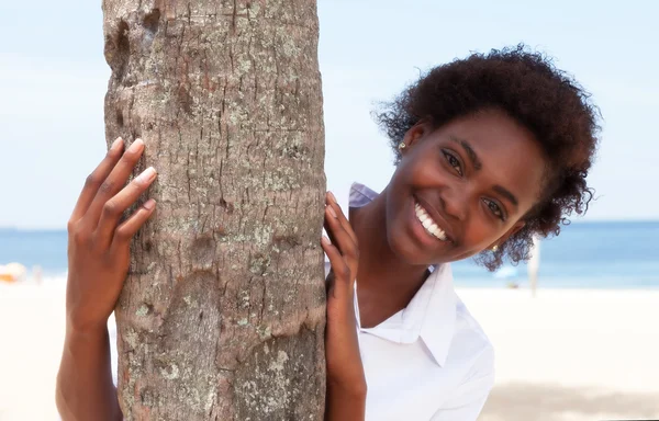 Lachende Afroamerikanerin hinter einem Baum Stockbild