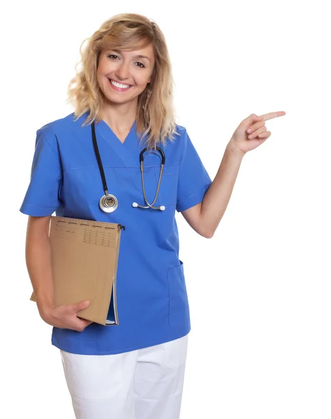 Hermosa enfermera con pelo rubio rizado y archivo médico señalando — Foto de Stock