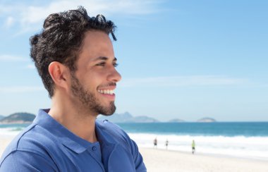 Guy with beard and blue shirt at beach looking sideways