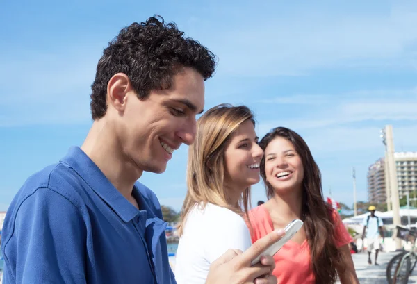 Mexican guy typing message at phone with two girlfriends — Stock Photo, Image