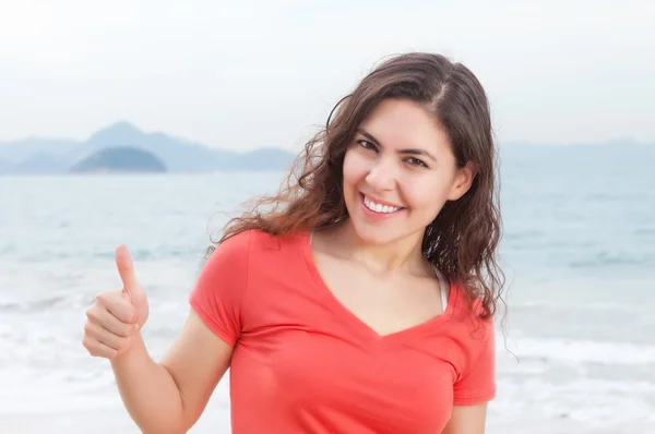 Young woman in a red shirt at beach showing thumb — Stock Photo, Image