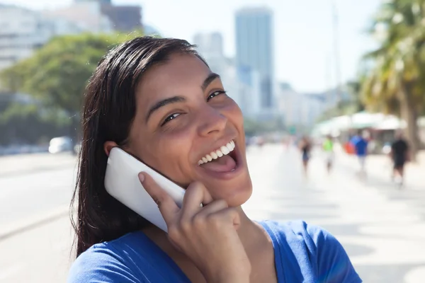 Lachende lateinische Frau mit langen dunklen Haaren am Telefon in der Stadt — Stockfoto