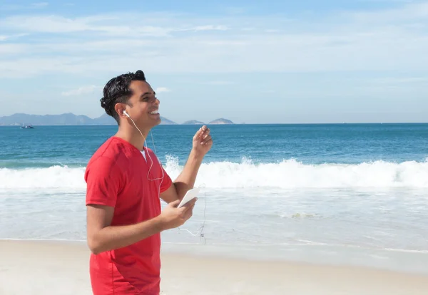Latin kille på stranden lyssna på musik på telefonen — Stockfoto