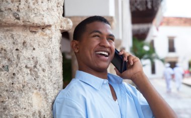 Happy latin guy with phone in a colonial town clipart