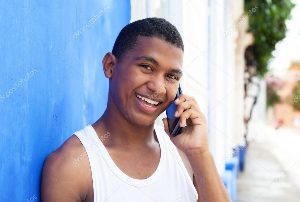 Happy latin guy at phone in front of a blue wall