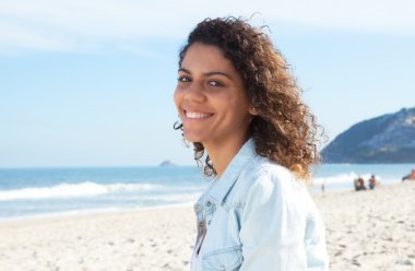 Kumsalda kıvırcık saçlı Latin kadın gülüyor