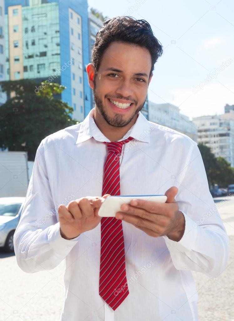 Laughing latin businessman in the city sending a message