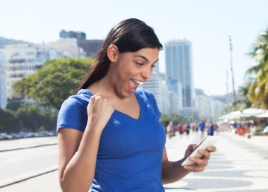 Cheering latin woman receiving good news on cellphone clipart
