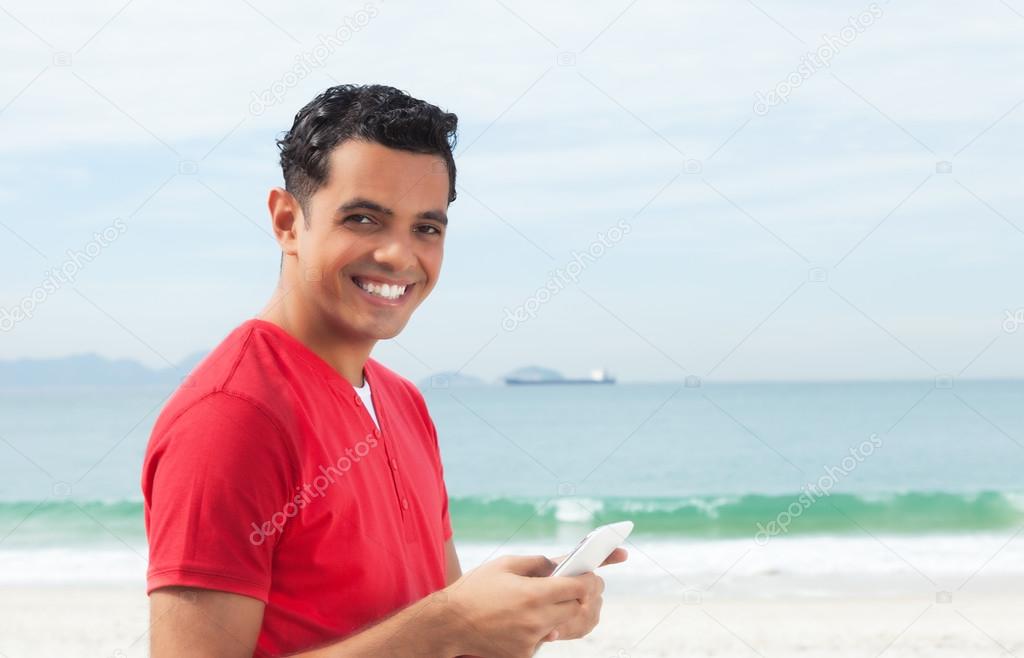 Laughing latin guy in red shirt writing message at phone