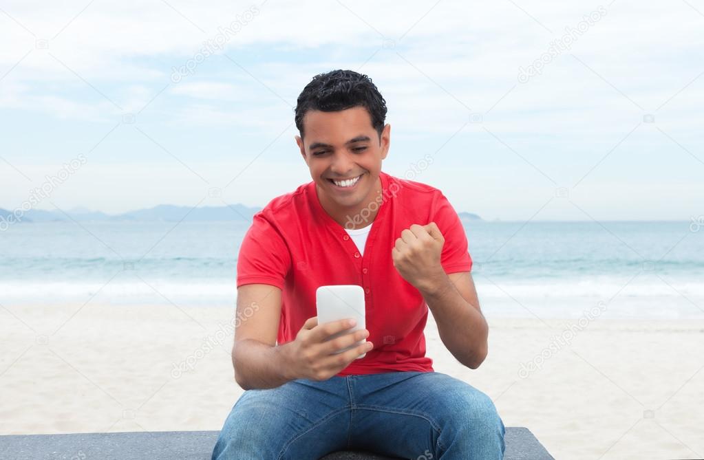 Happy latin guy in red shirt looking at phone