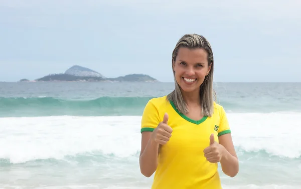 Rubia brasileña deportes ventilador mostrando pulgares en la playa —  Fotos de Stock