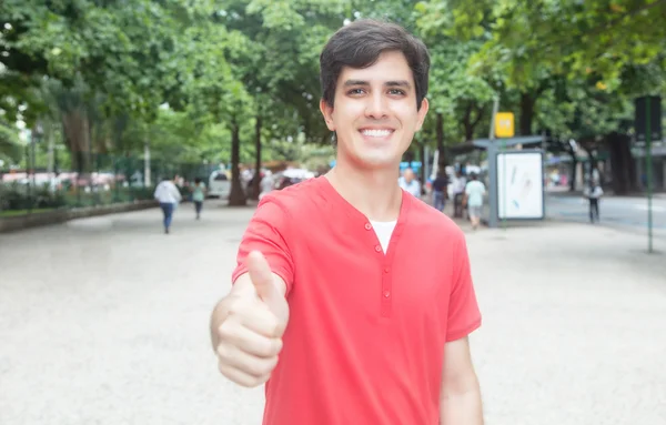Caucasian guy with red shirt in city showing thumb — Stock Photo, Image