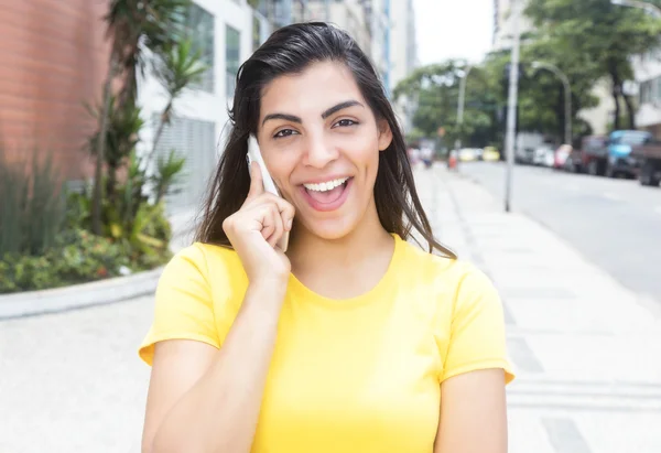 市に電話で黄色のシャツを持つラテン女性を笑ってください。 — ストック写真