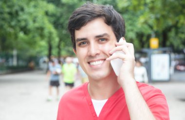 Kırmızı gömlekli yakışıklı beyaz adam bir parkta telefon ile