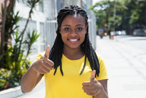 Mujer afroamericana con camisa amarilla en la ciudad mostrando el pulgar — Foto de Stock